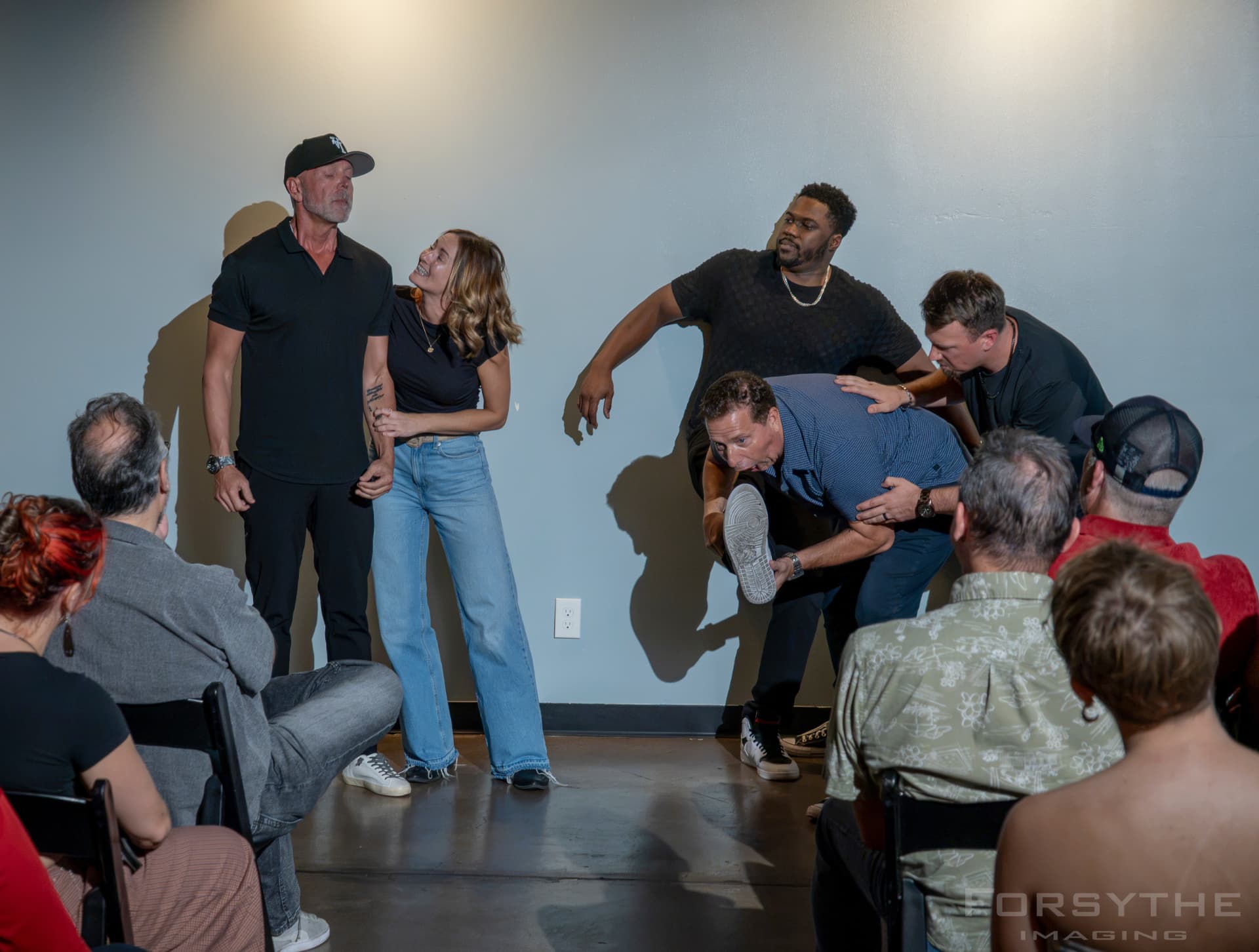 Improv troupe frozen mid-scene in front of a packed room