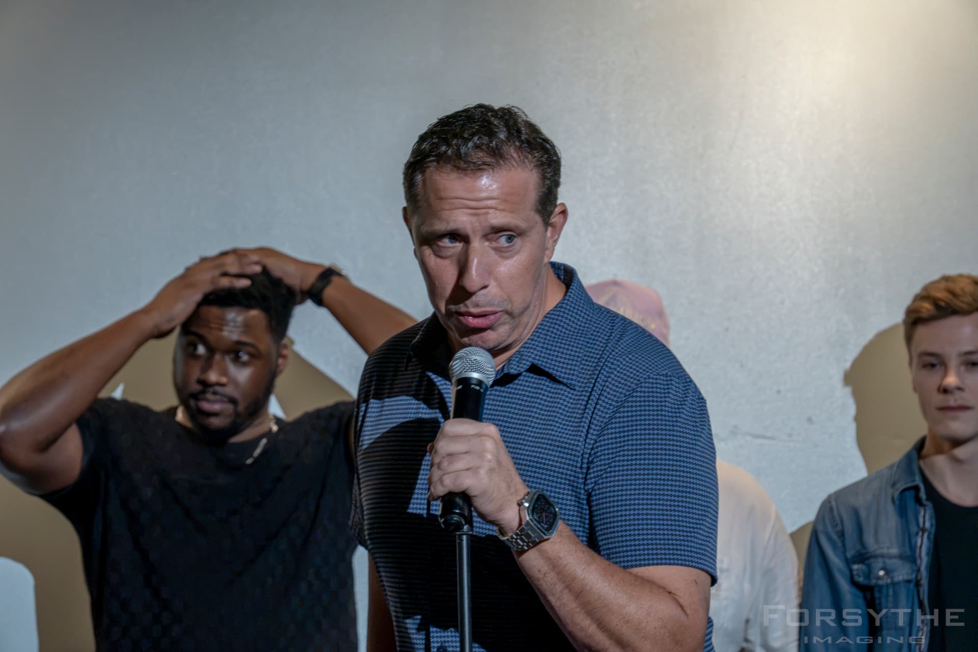 Comedian on the mic with the lineup reacting behind him